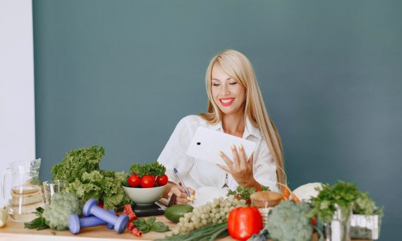 Woman using a tablet surrounded by fresh vegetables at a table, showcasing healthy lifestyle and technology.