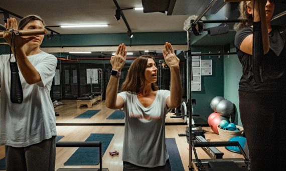 Pilates instructor guiding two women during a workout in a modern gym environment.