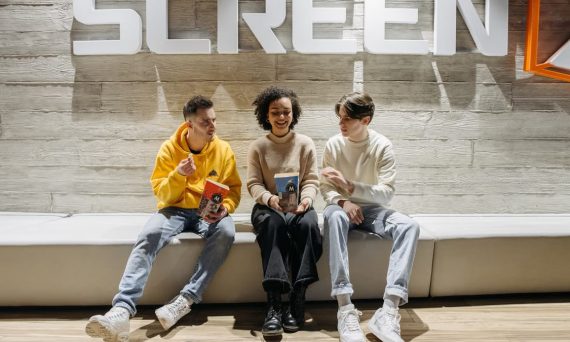 Three young adults sitting under cinema signage, enjoying snacks and conversation.